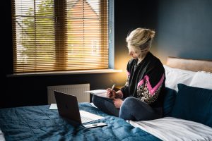 Young woman with a laptop sitting on her bed and taking notes. 